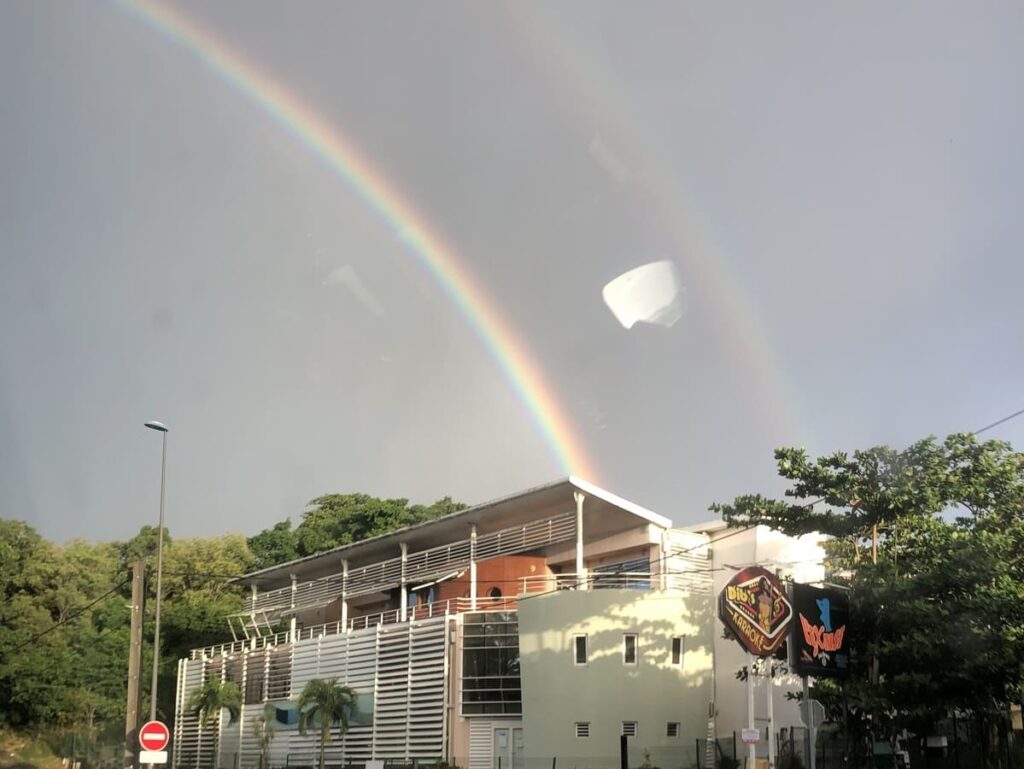 An image showing a vibrant rainbow on a street in Guadeloupe. Rainbows are a stunning natural occurrence that appear when sunlight is refracted and dispersed through water droplets in the atmosphere. This image is part of a post that explains how rainbows are formed, including the science behind their colors and the various types of rainbows that can be seen in the sky.